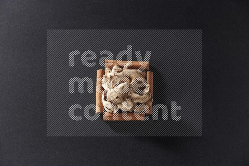 A single square of cinnamon sticks full of dried ginger on black flooring
