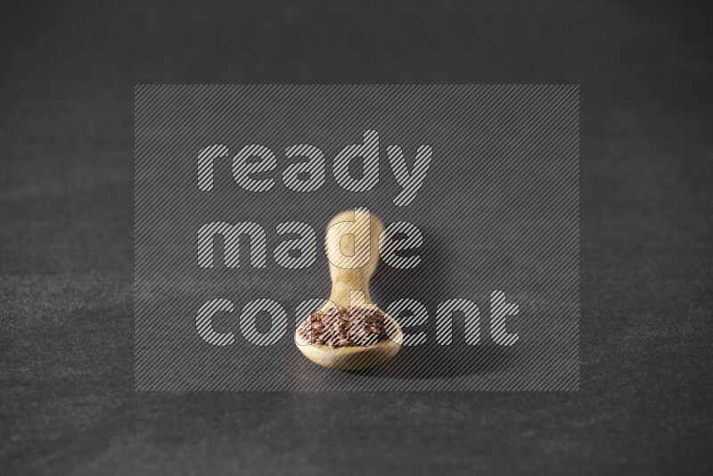 A wooden spoon full of flaxseeds on a black flooring