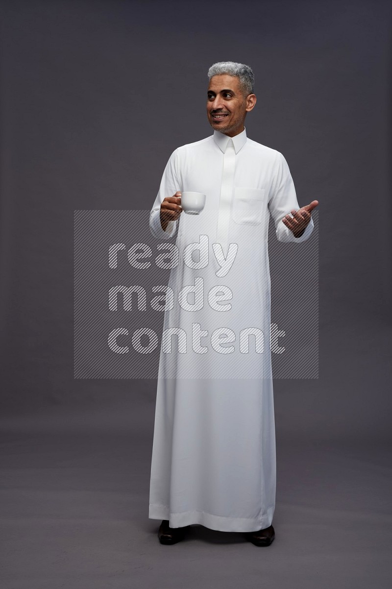 Saudi man wearing thob standing holding mug on gray background