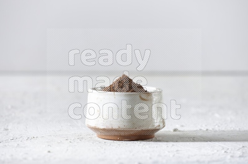 A beige ceramic bowl full of cloves powder on a white flooring