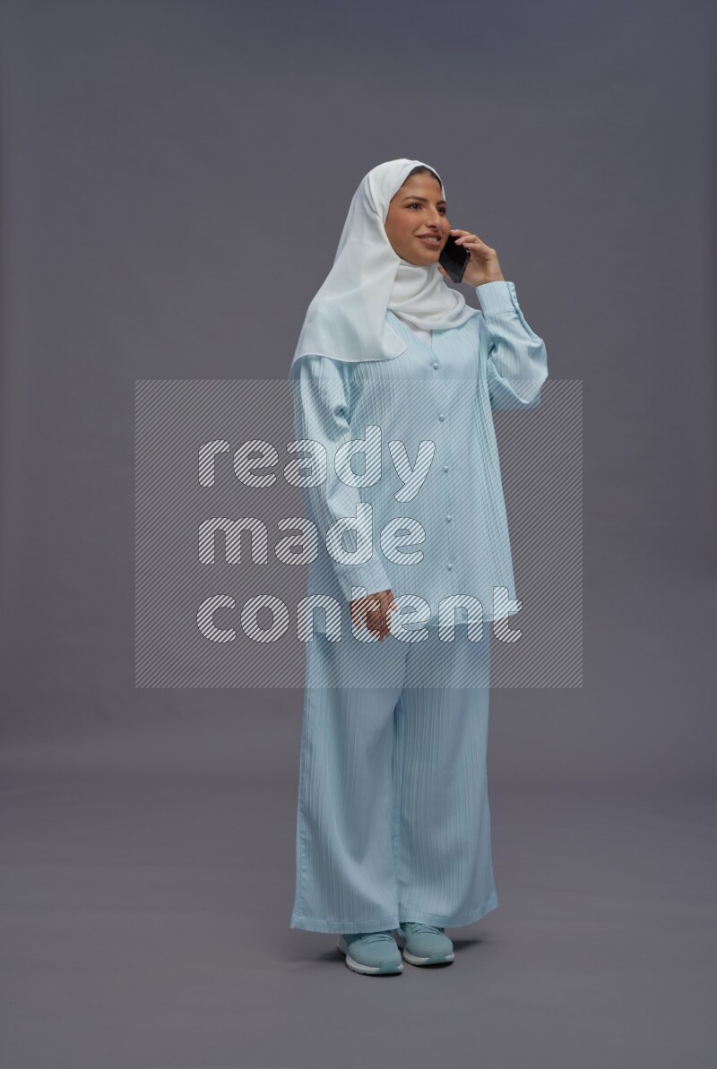 Saudi woman wearing hijab clothes standing talking on phone on gray background