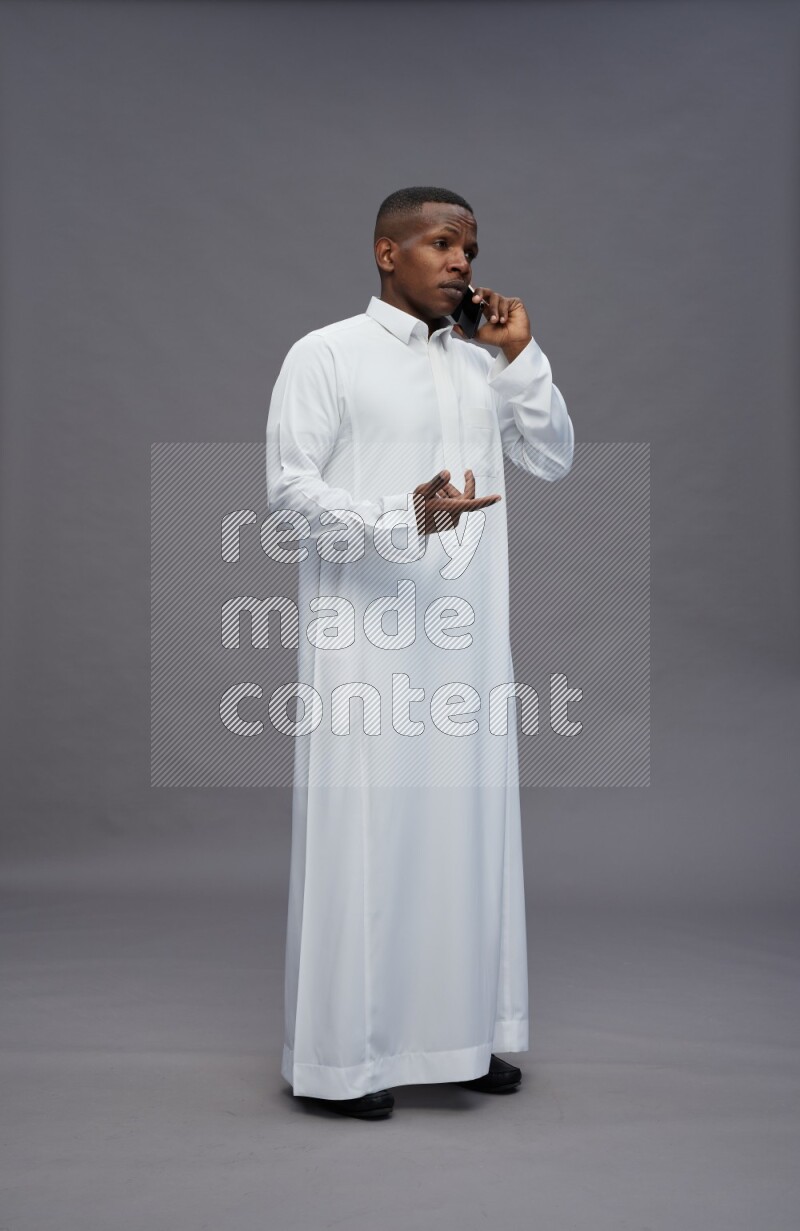 Saudi man wearing thob standing talking on phone on gray background
