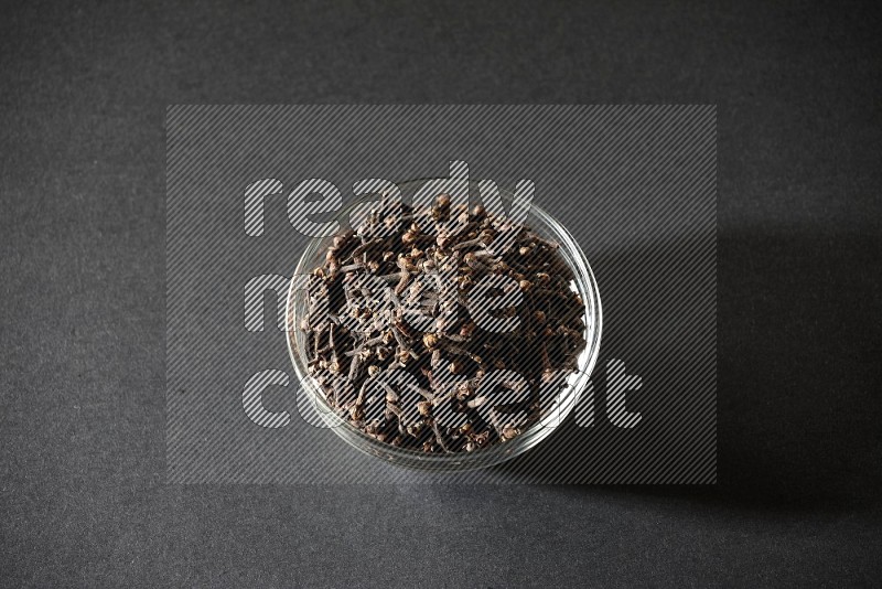 A glass bowl full of cloves on a black flooring