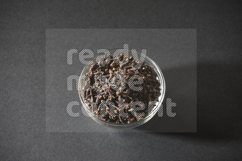 A glass bowl full of cloves on a black flooring