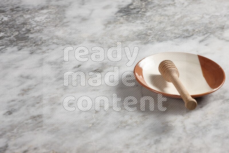 Multicolored pottery plate with wooden honey dipper in it on grey marble background