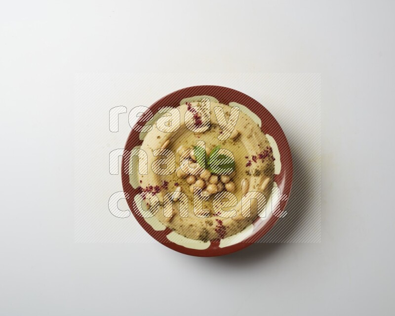 Hummus in a traditional plate garnished with zaatar & sumak on a white background
