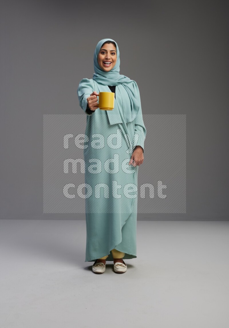 Saudi Woman wearing Abaya standing  holding a mug on Gray background