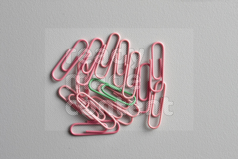 A green paperclip surrounded by bunch of pink paperclips on grey background
