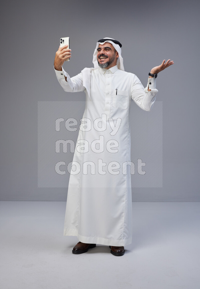 Saudi man Wearing Thob and white Shomag standing taking selfie on Gray background