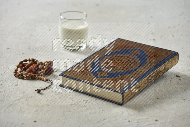 Quran with dates, prayer beads and different drinks all placed on textured white background