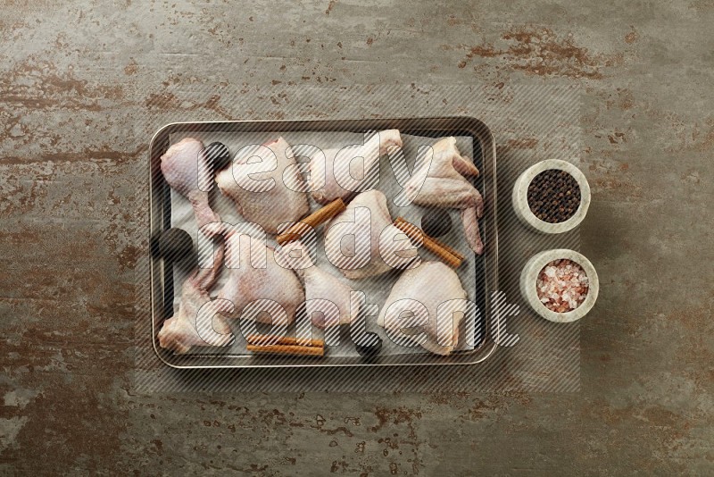 Mixed fresh chicken pieces in an oven tray on a textured rustic background