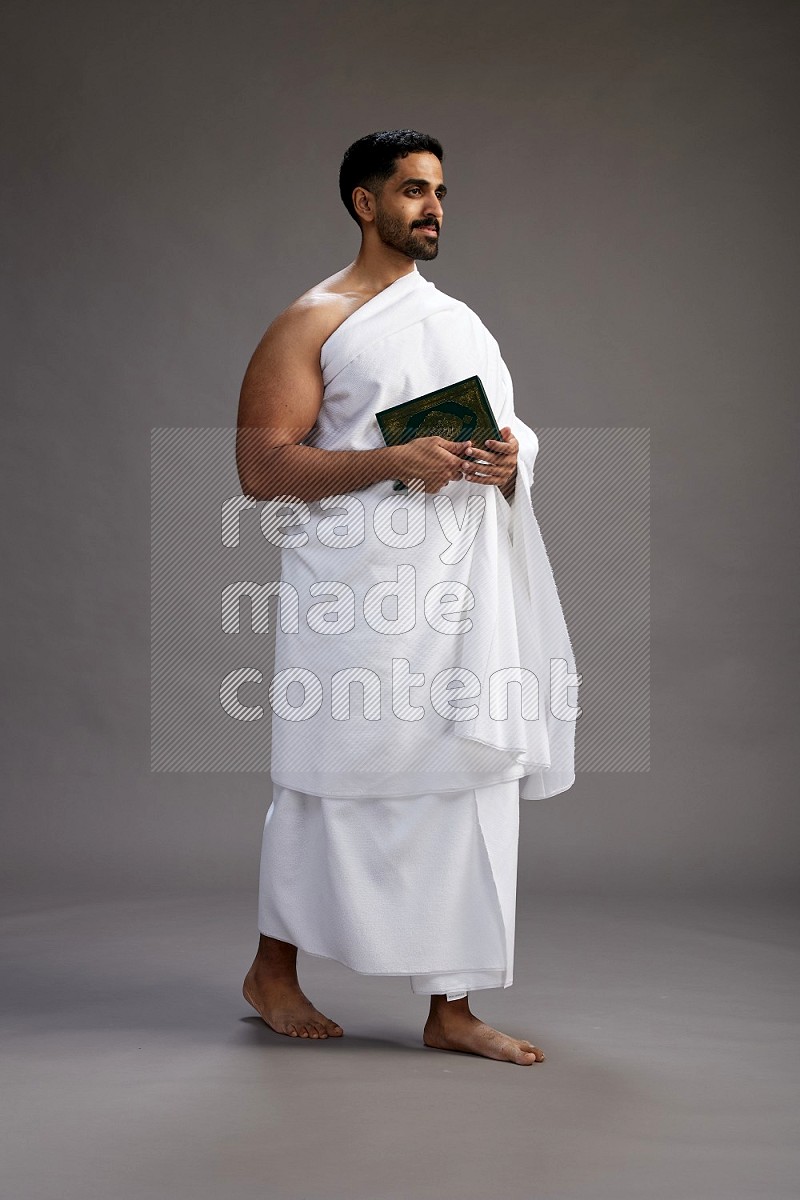 A man wearing Ehram Standing reading quran on gray background