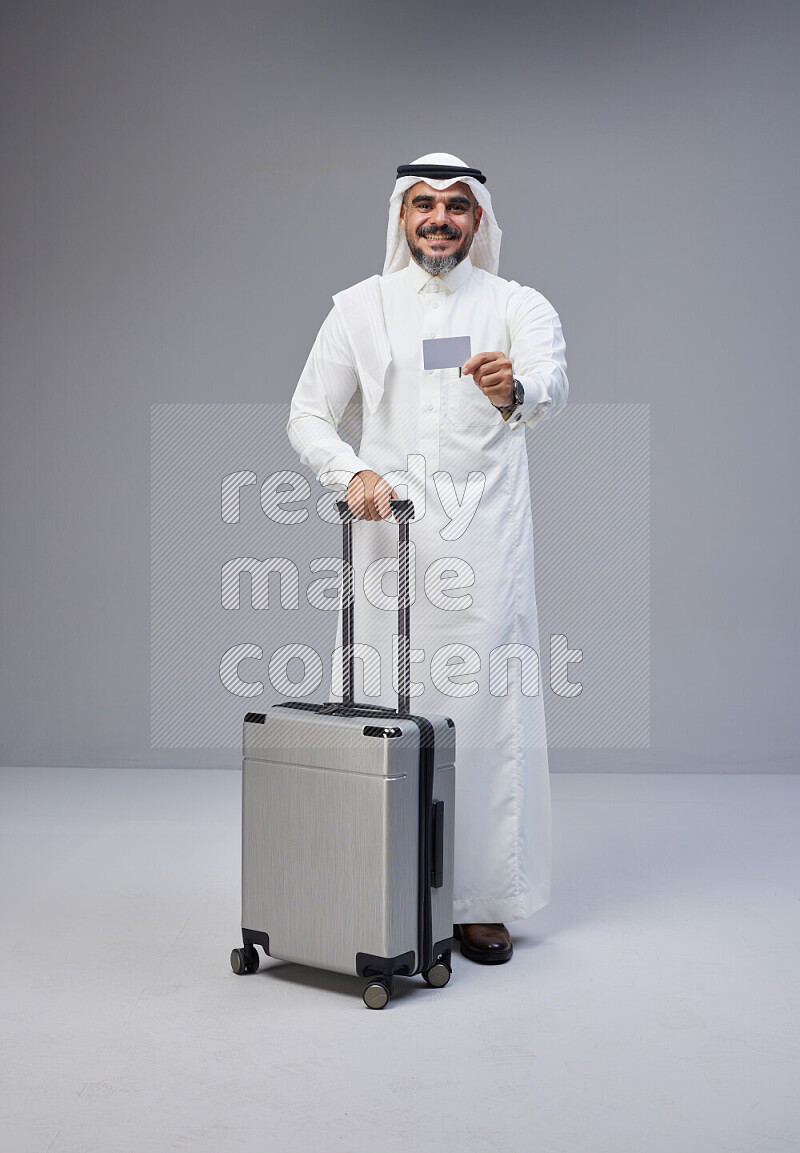 رجل سعودي يرتدي ثوب ابيض ويحمل بطاقة بنكية وبجواره حقيبة سفر