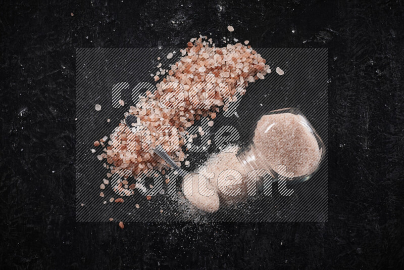 A glass jar full of fine himalayan salt with some himalayan crystals beside it on a black background