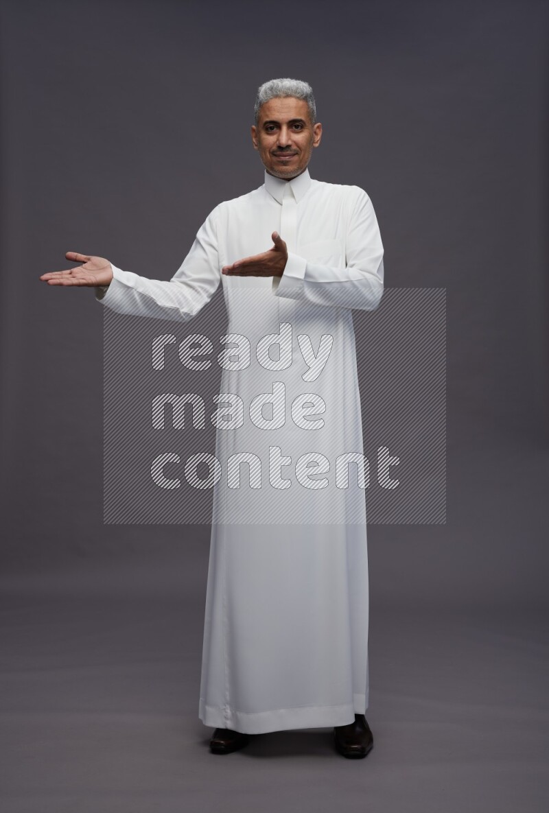 Saudi man wearing thob standing interacting with the camera on gray background