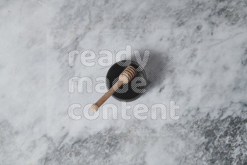Black pottery bowl with wooden honey dipper in it on grey marble background