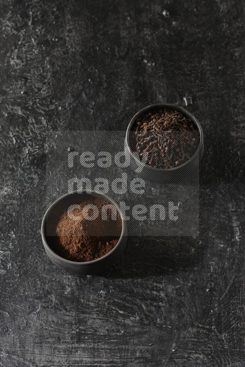 وعاءين من الفخار الأسود أحدهما ممتلئي بحبوب القرنفل والآخر ممتلئ ببودرة القرنفل على خلفية سوداء