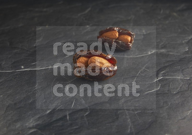 two almond stuffed madjoul dates on a black textured background