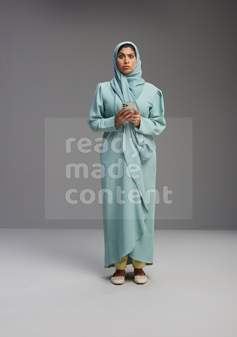 Saudi Woman wearing Abaya standing texting on phone on Gray background