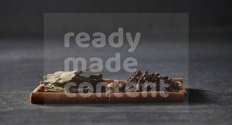 مربعان من أعواد القرفة ممتلئان بالقرنفل وأوراق الغار علي خلفية سوداء