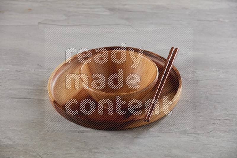 brown wood round bowl on top of brown wood round plate and wood chopsticks, on grey textured countertop