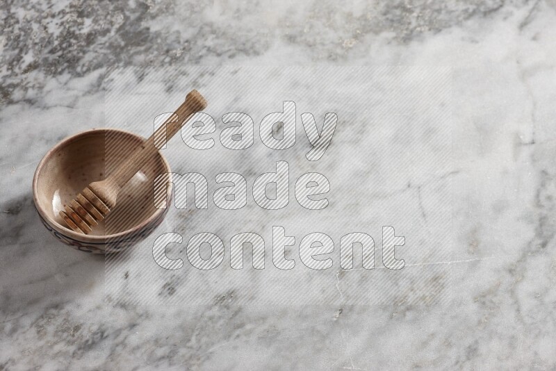Decorative pottery bowl with wooden honey dipper in it on grey marble background