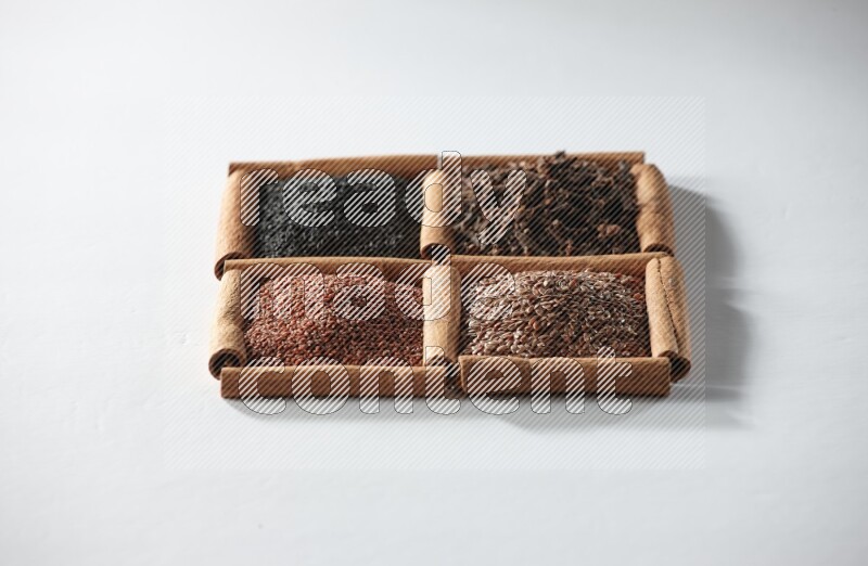 4 مربعات من أعواد القرفة ممتلئة بحبة البركة والقرنفل وبذور الكتان وحب الرشاد على أرضية بيضاء