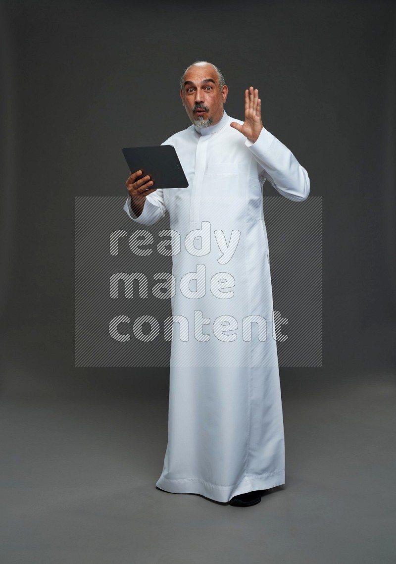 Saudi man without shomag Standing working on tablet on gray background