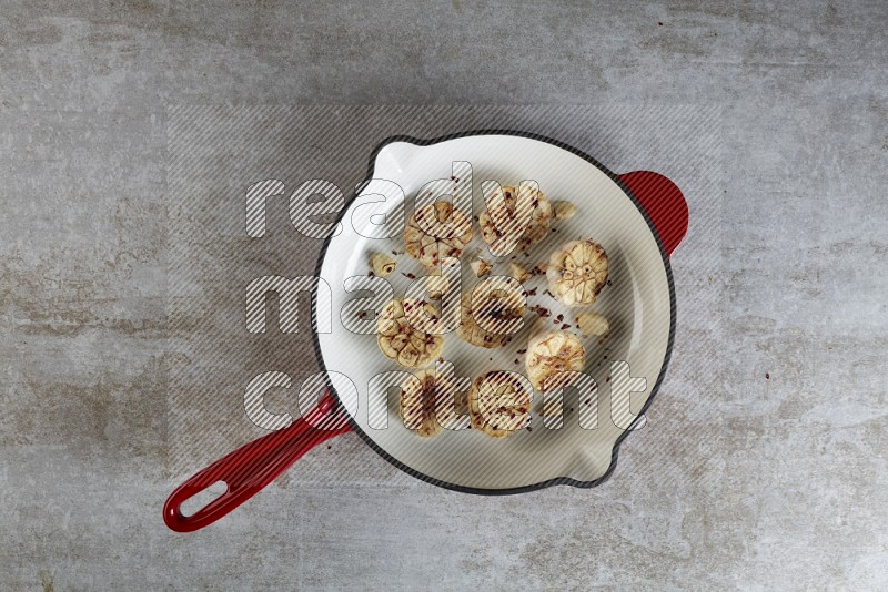 half's roasted garlic in a red-coated cast iron pan on a grey textured countertop