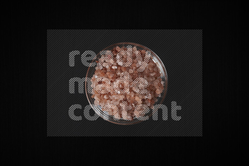 A glass bowl full of coarse himalayan salt crystals on black background