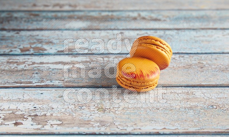 45º Shot of two orange Exotic macarons on light blue wooden background