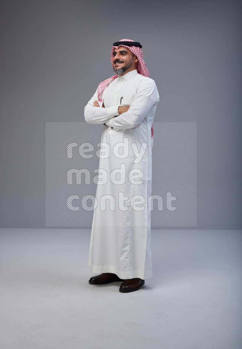 Saudi man Wearing Thob and red Shomag standing with crossed arms on Gray background