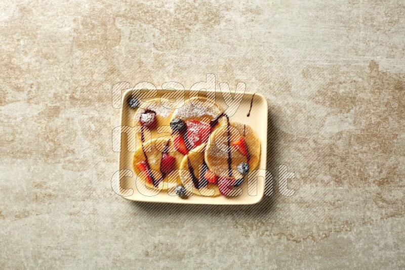 Five stacked mixed berries mini pancakes in a rectangular plate on beige background