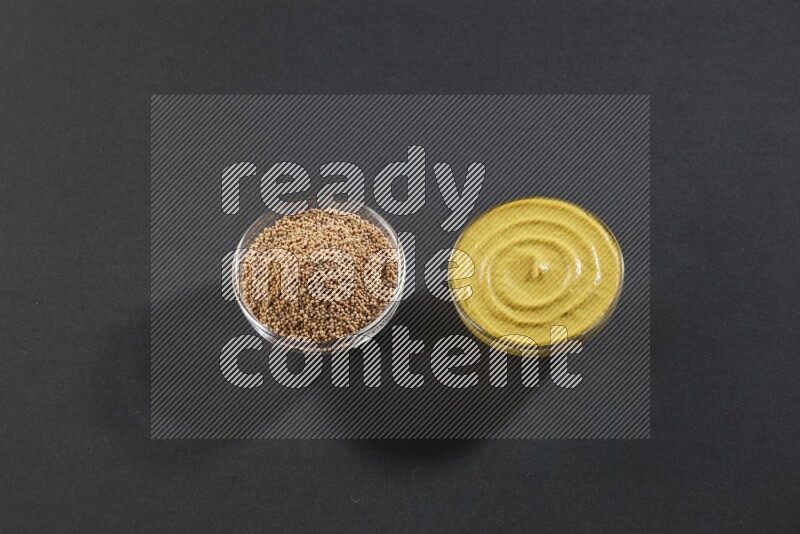 2 glass bowls, one full of mustard seeds and the other full of mustard paste on black flooring