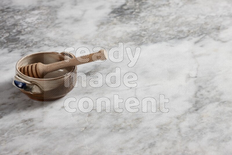 Multicolored pottery bowl with wooden honey dipper in it on grey marble background
