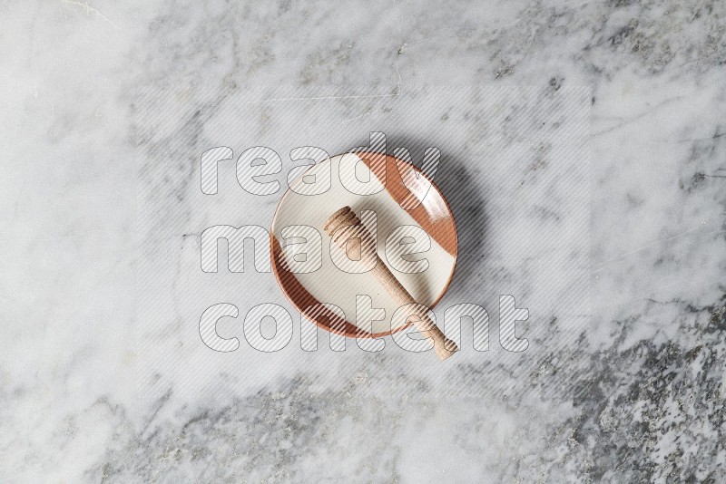 Multicolored Pottery Plate with wooden honey handle in it, on grey marble flooring, Top View