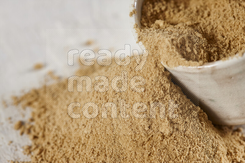 A beige pottery bowl full of ground ginger powder with fallen powder from it on white background