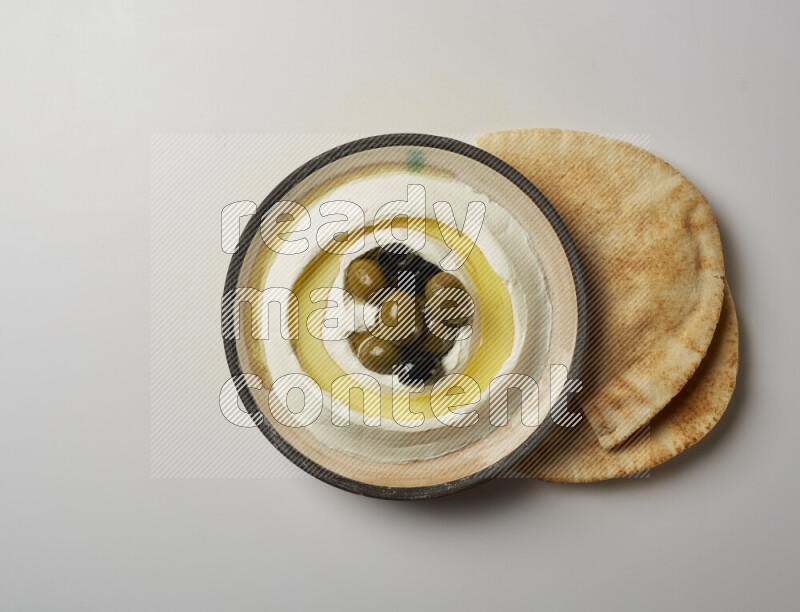 Lebnah garnished with whole black olives in a pottery plate on a white background