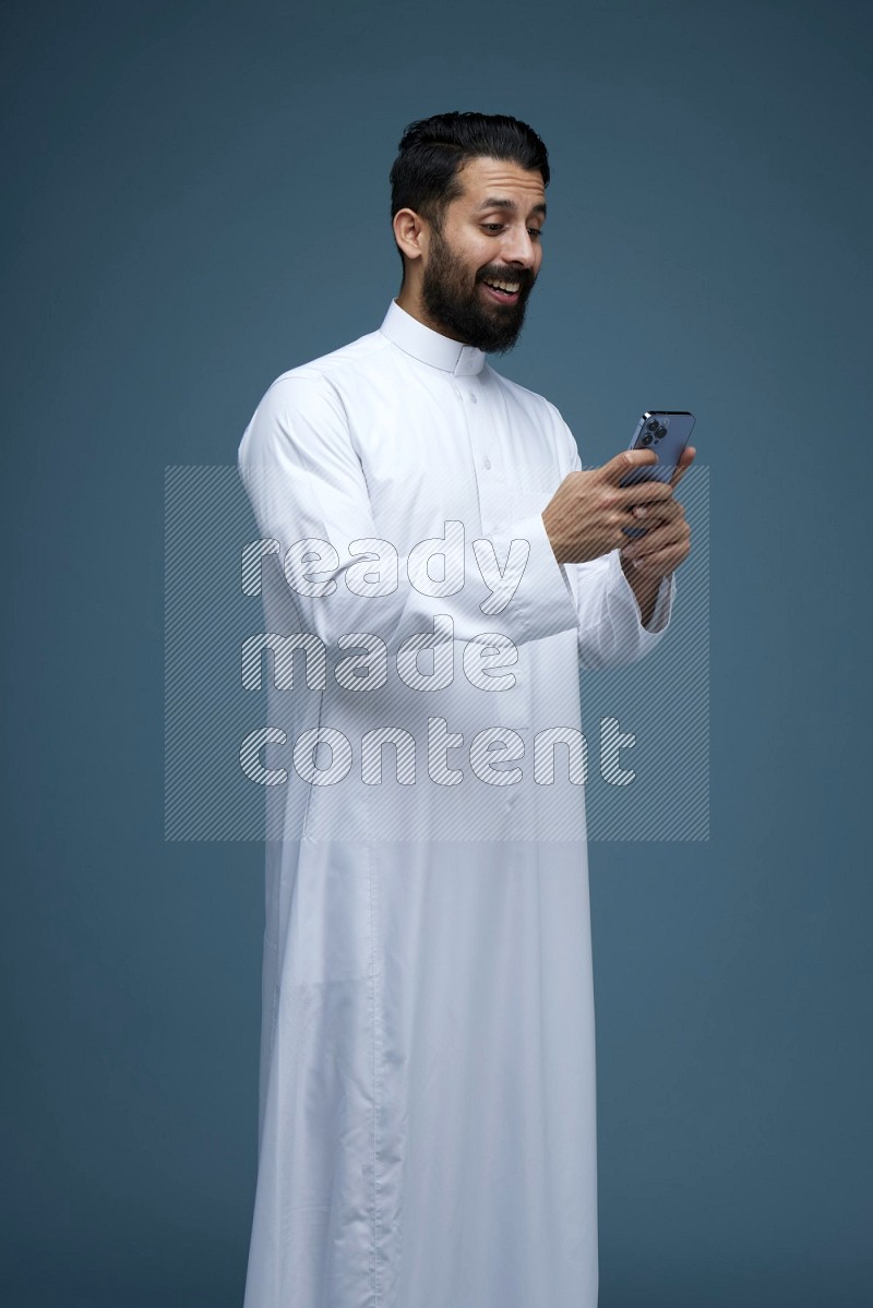 A man Texting in a blue background wearing Saudi Thob