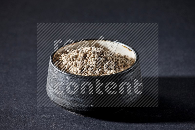 Black pottery bowl full of white pepper on black flooring