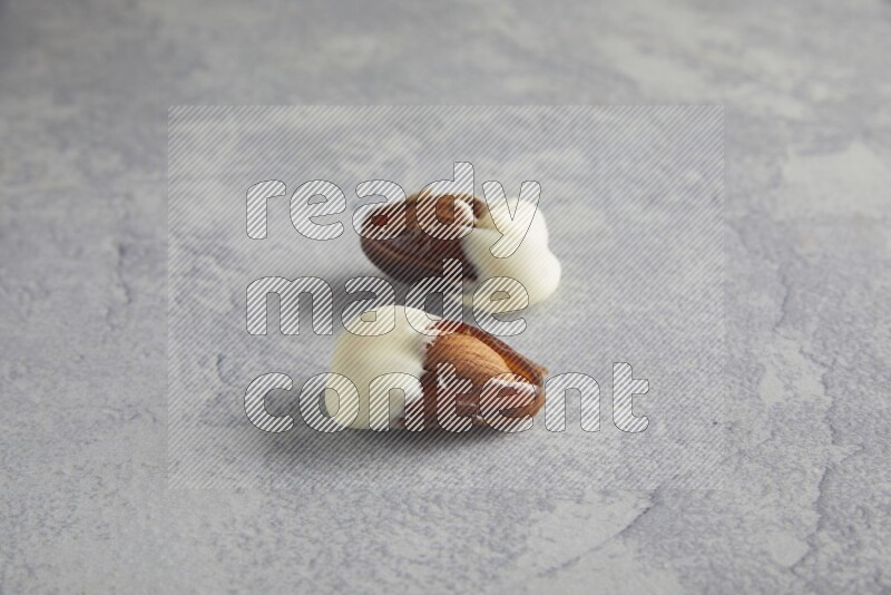 two almonds stuffed dates covered with white chololate on a light grey background