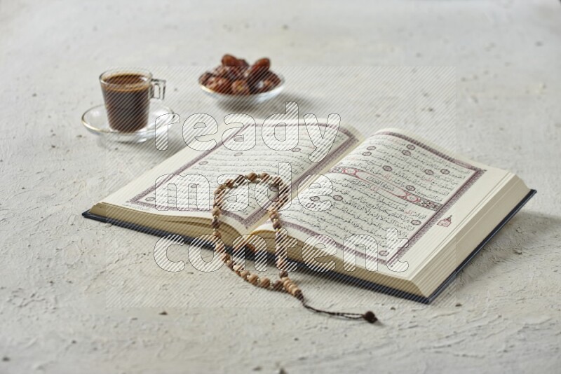 Quran with dates, prayer beads and different drinks all placed on textured white background