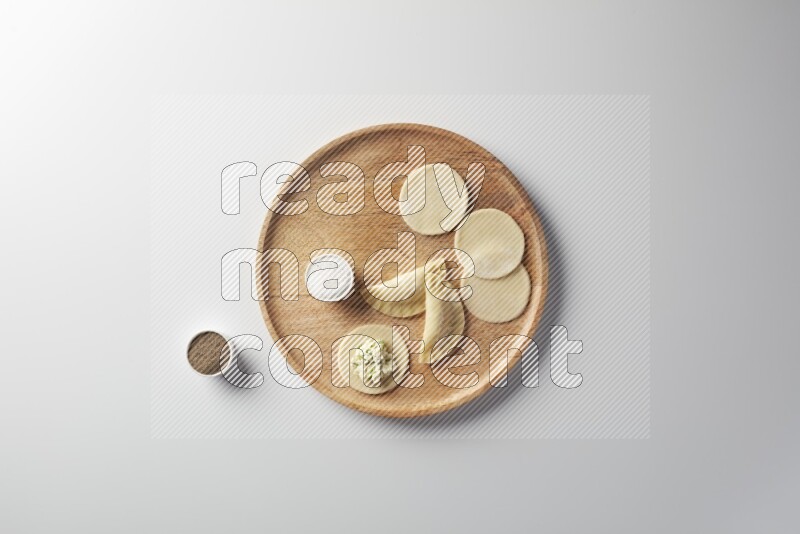 two closed sambosas and one open sambosa filled with cheese while salt, and black pepper aside in a wooden dish on a white background