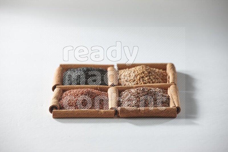 4 مربعات من أعواد القرفة ممتلئة بحبة البركة وبذور الخردل وبذور الكتان وحب الرشاد على أرضية بيضاء