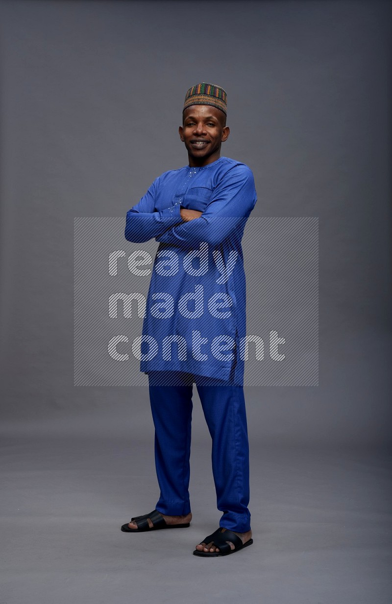 Man wearing Nigerian outfit standing with crossed arms on gray background