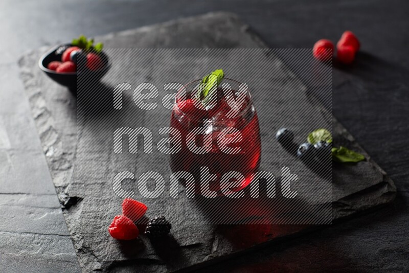 A glass of mixed berries juice with mint leaves on black background