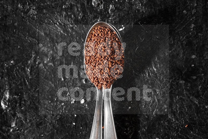 2 metal spoons full of garden cress seeds on a textured black flooring