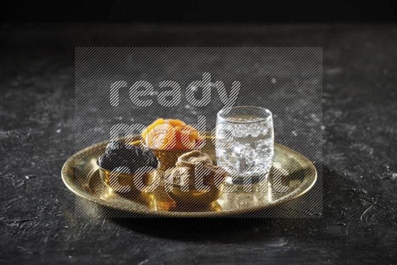 Dried fruits in metal bowls with water on a tray in dark setup