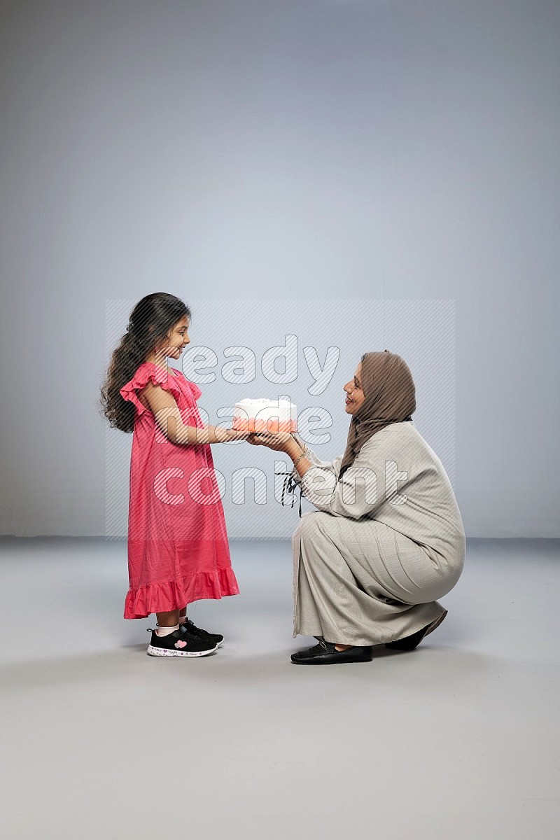 A mother giving a cake to her daughter on gray background