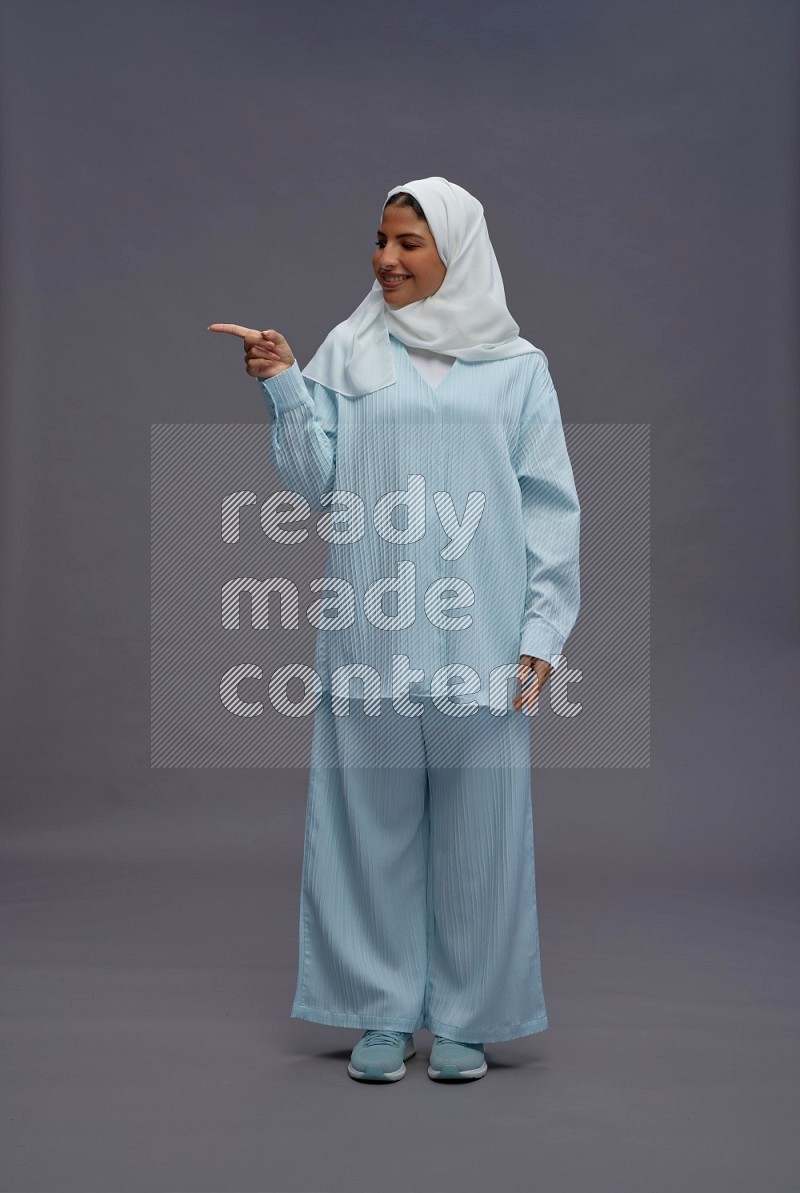 Saudi woman wearing hijab clothes standing interacting with the camera on gray background